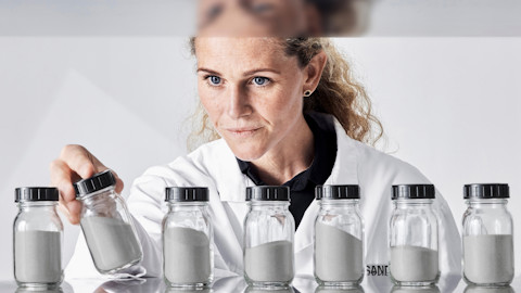 Metal powder expert in white lab coat, looking at metal powders in glass jars